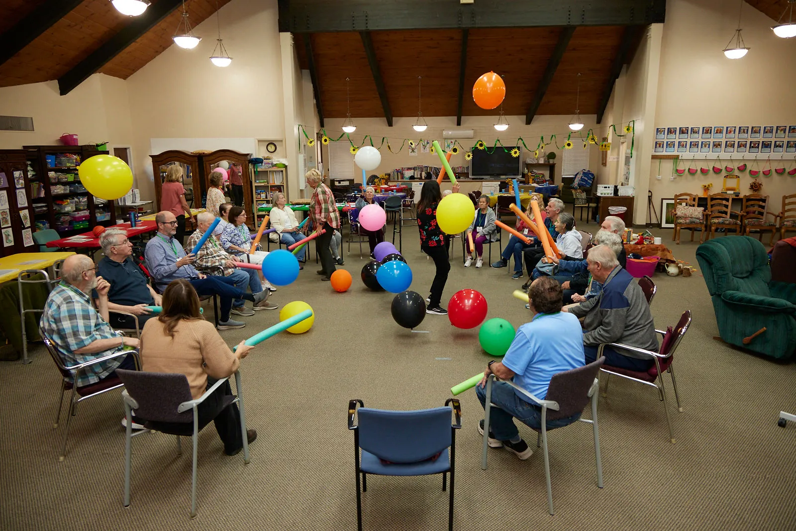 Participants in a circle enjoy a seated balloon-and-noodle game at Aspen Senior Day Center