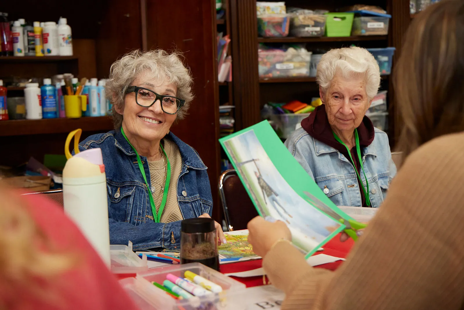 Two participants smile over a picture book during a craft activity at Aspen Senior Day Center